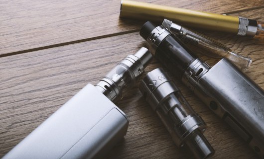 Three e-cigarettes and components are fanned out on a wooden surface.