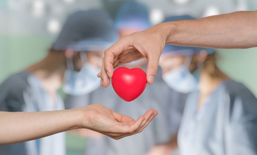 Someone passes a red, 3D heart to another as three surgeons work in the background.