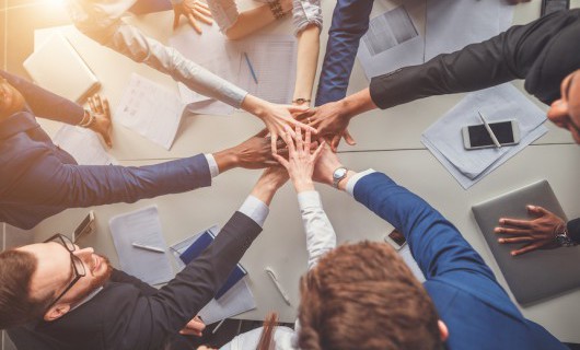 Eight people each put a hand into the middle of a table, one on top of another.