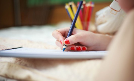 A pot of bright pencils sits blurred behind someone's hand drawing with a blue pencil.