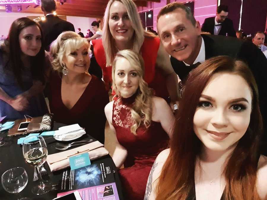 Changemakers and Kelly's husband Graham, sit around a table, posing for a selfie.