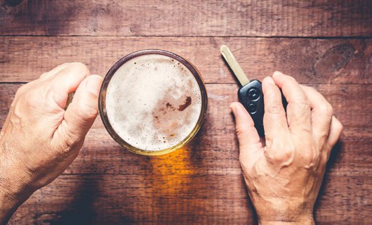 Someone is holding a pint of beer and car keys on top of a table.