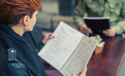 A woman sits at a table with a man, staring at the menu in her hand.