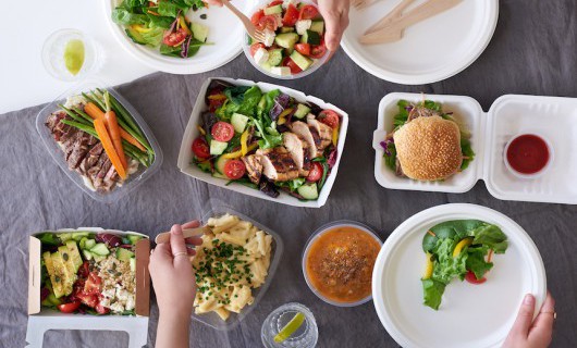 Hands reach for a range of colourful, healthy food dishes, including salads and pasta.