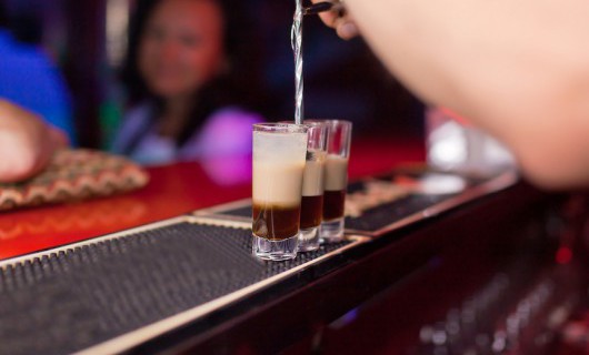 Three tall shot glasses are being filled at a bar.