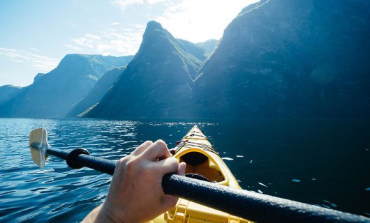 A man canoeing in a lake with a scenic mountain range background.