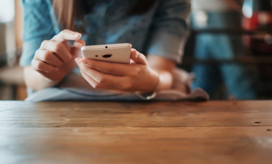 A woman sits at a table, using the phone in her hands.