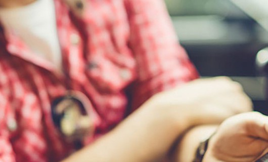 A blurred image of a man sat in the car, holding his phone out to share what's on the screen.