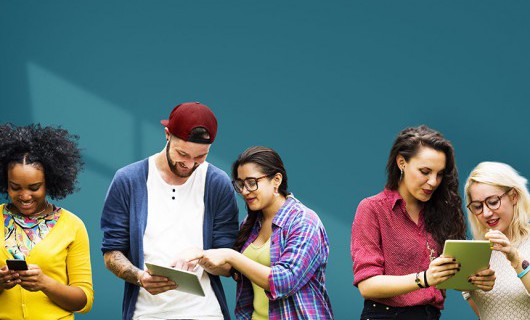 One young man and four young women using tablets and mobile phones between them.