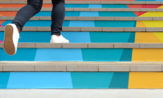 Two feet in plimsols walk up a set of colourfully painted stone steps.