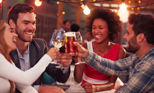 Two men and two women laughing and having a drink at a table in a bar.