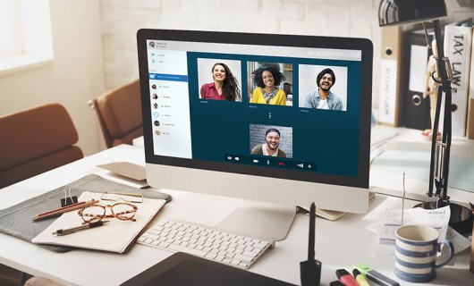 A computer screen on a desk with four people on a video call on the screen.